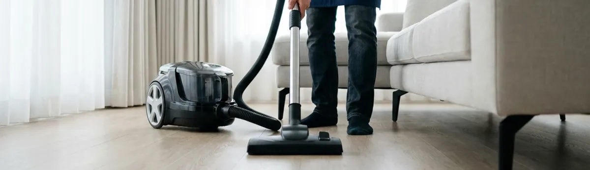 Professional house cleaner vacuuming a living room floor with a canister vacuum cleaner, Chula Vista, CA.