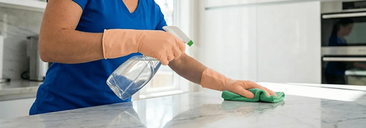Maid service worker spraying and wiping a kitchen countertop with a microfiber cloth for sanitizing, Chula Vista, CA.